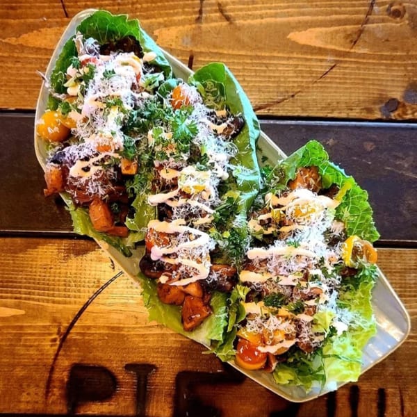 Three lettuce wraps filled with roasted vegetables, drizzled with sauce, and sprinkled with cheese and herbs.