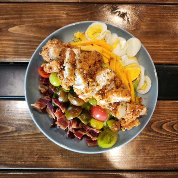 Crispy fried chicken salad with bacon, tomatoes, hard-boiled eggs, and mango slices.