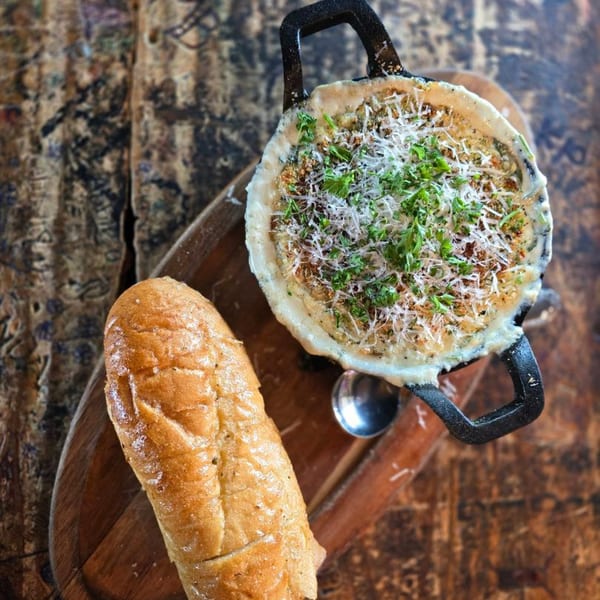 Creamy dip in a cast iron skillet with shredded cheese and parsley, served with bread.